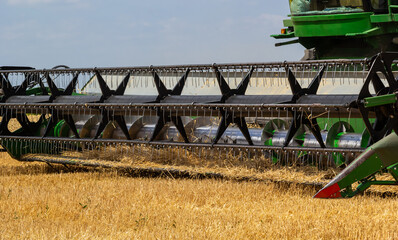 Combine harvester harvests ripe wheat. Ripe ears of gold field on the cloudy sky background. ....