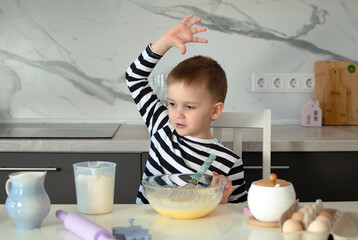 5-year-old boy is playing with dough in kitchen. Child bakes cookies. Portrait of child smiling cheerfully and kneading baking dough. Children learn new things. Concept of children's leisure
