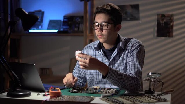 Engineer student inspecting disassembled broken motherboard use laptop with repair video. Technology microelectronics science education
