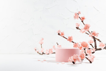 Fresh lush pink sakura flowers on branch with cylinder podium mockup in soft light white interior on table in floral spring style for presentation cosmetic products, goods, branding, copy space. © finepoints
