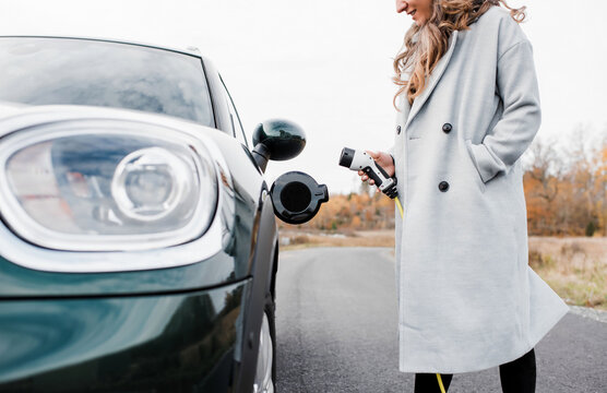 women smiling plugging in an electric car on a country road