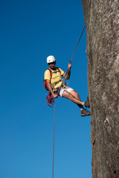 Man rappelling steep rocky mountain with blue sky on the back