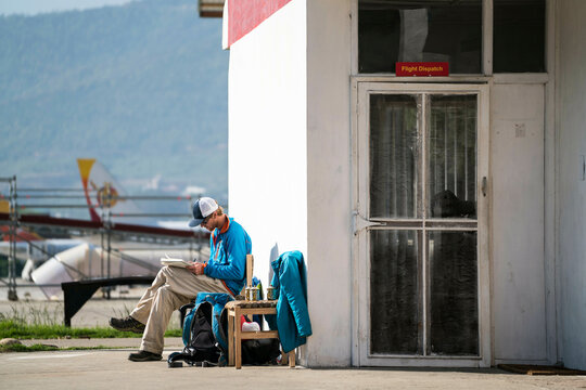 Man sits outside of flight dispatch office writing in Bhutan