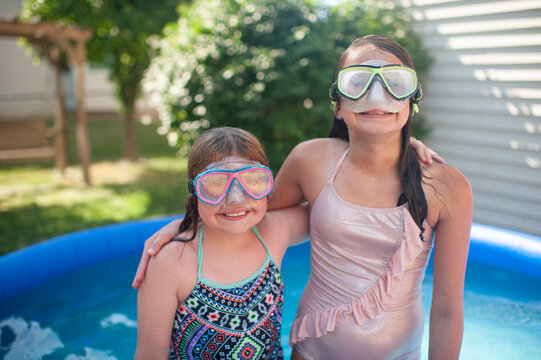 Tween girls 10-12 wearing swimming goggles with arms around each other