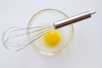 Metal whisk and chicken yolk in a glass bowl