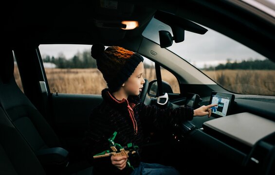 Young Boy Sat In The Drivers Seat Of An Electric Car Using Sat Nav