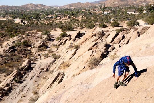 boy climbing down steep large rocks in desert