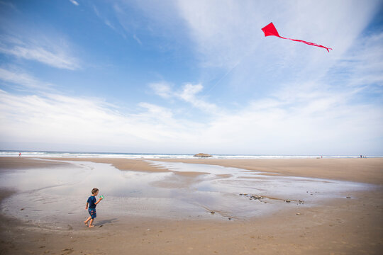 Toddler boy flying red kite at beach.