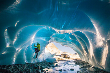 Man ice climbs inside glacial cave during helicopter adventure tour.