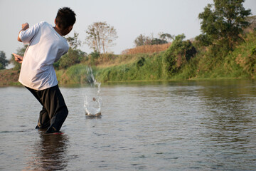 Asian boy is spending his freetimes by diving, swimming, throwing rocks and catching fish in the river happily, hobby and happiness of children concept, in motion.