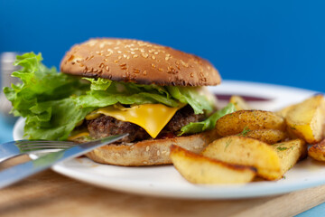 Homemade imperfect burger with potatoes and salad on a plate. Food on the table in a white plate on a wooden board