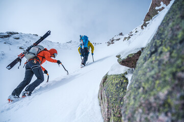 Two men climbing steep snow gully with skis