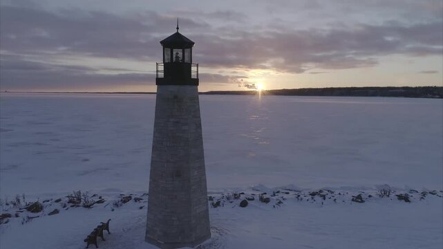 Dolly shot of lighthouse by frozen lake against cloudy sky during sunset
