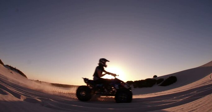 Competitive quad biker kicking up a plume of sand while racing over a sand dune