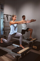Young woman and man exercising in a gym with personal trainer on pilates machine.