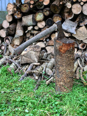 An axe stuck in a firewood log. Lot of firewood logs in blurred background.