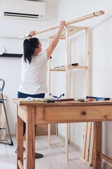 Woman assembling new wooden shelf and furniture in the apartment.