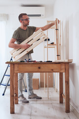 Man assembling new wooden shelf and furniture in the apartment.