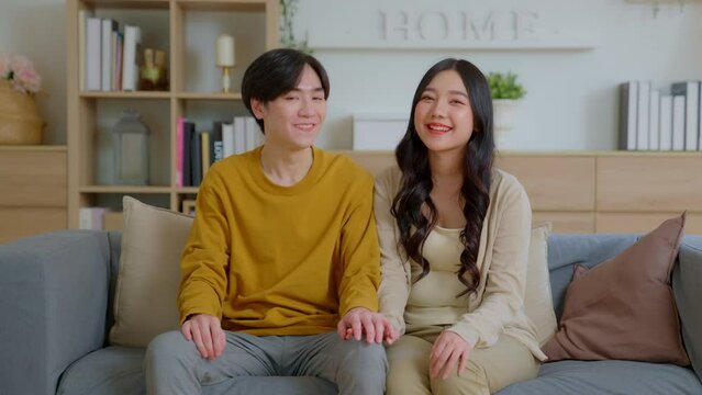 Happy asian young family couple in new home on moving day, First time real estate owners man husband embrace woman wife look and smile happily for the camera in living room of new home.