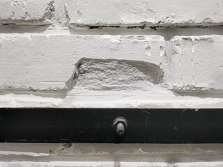 Brick wall painted with white paint. Regular brickwork. Black steel strip over white brick.