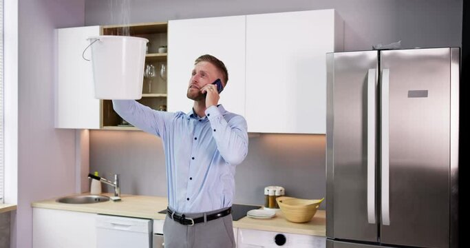 Man Calling Plumber While Collecting Water Leaking From Ceiling