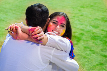 Happy young indina woman hug her husband while celebrating holi with colorful powder or gulal.