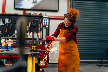 A self-employed worker is cutting a metal beam using a grinder, she is focused on her work and...