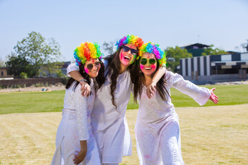 Group of playful young indian female friends wearing white kurta and colorful hair wigs celebrating...