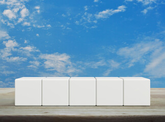 Five white block cubes on wooden table over blue sky with white clouds