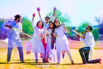 Fototapeta Group of happy young Indian people celebrating holi festival at park outdoor, Playful adult male and friends with colorful paint faces playing with gulal. obraz