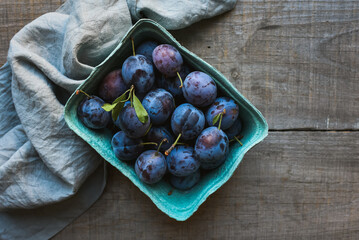 Top view of carton of fresh picked plums on wooden background.