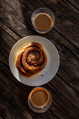 A sticky bun in the sunlight on a wooden table and two cups of coffee.