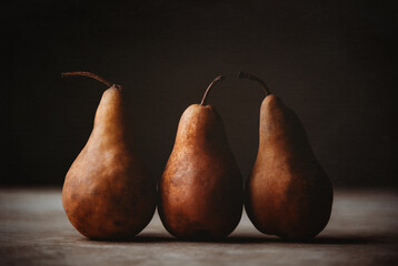 Close up of three brown bosc pears against dark background.