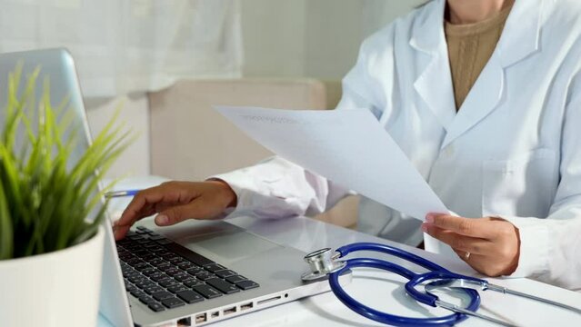 Doctor or nurse woman in uniform with stethoscope working she typing information of patient prescription from paperwork medical history form into laptop computer for record document data report