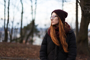 red-haired woman in a hat and down jacket in the middle of the park