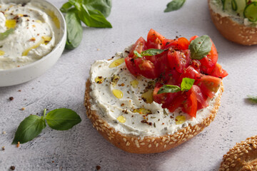Fresh bun with sesame seeds with cheese cream and fresh tomatoes with basil leaves close up