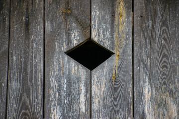 Wycięty otwór o kształcie rombu w starych drewnianych drzwiach 