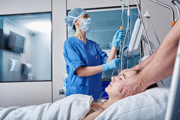 Two doctors checking on unconscious woman patient at intensive care unit and monitoring her health with medical equipment and sensors. ICU