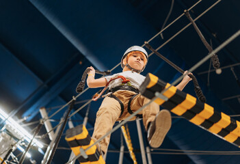cute little boy climbing in adventure park passing obstacle course. high rope park indoors
