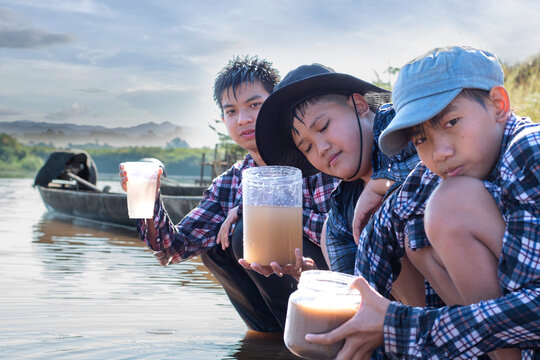 Asian boys holding magnifying glass and transparent plastic tubes to to the experiment of water from local river to study the fertility of the river and environmental problems around their villages.