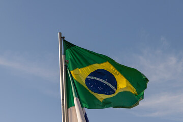 Flag of Brazil, fluttering in the wind, with blue sky in the background. Selective focus.