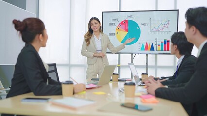 Asian businesswoman leader uses presentation on TV with statistics and discussing with businesspeople group office meeting