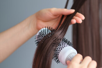 Drying brunette hair with hair dryer and round brush. hair care at home