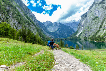 Fototapeta na wymiar Man is sitting, hiking at Obersee am Königssee. beautiful Bavarian Landscape Behind and between the Koenigssee and Obersee
