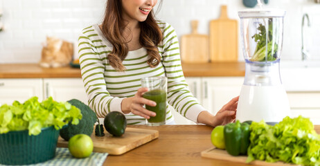 Portrait of beauty healthy asian woman making green vegetables detox cleanse and green fruit smoothie with blender.young girl drinking glass of green fruit smoothie in kitchen.Diet concept.healthy