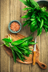 Fresh wild leek leaves on a wooden board. Leaves of fresh ramson with pink Himalayan salt