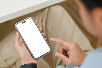 Over shoulder closeup view of young man sitting at office desk and using mobile phone