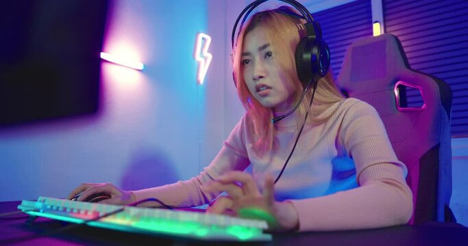 Young player woman wearing gaming headphones intend to do playing live stream games online at home, Happy Gamer endeavor plays online video games tournament with computer desktop with neon lights