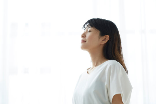 明るい窓際で目を閉じて立つ笑顔の女性