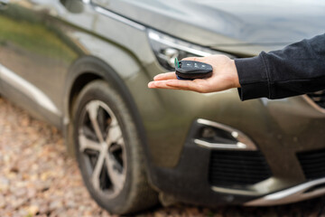 Person holding a car key in the hand stands front car. Insurance, loan and buying car concept